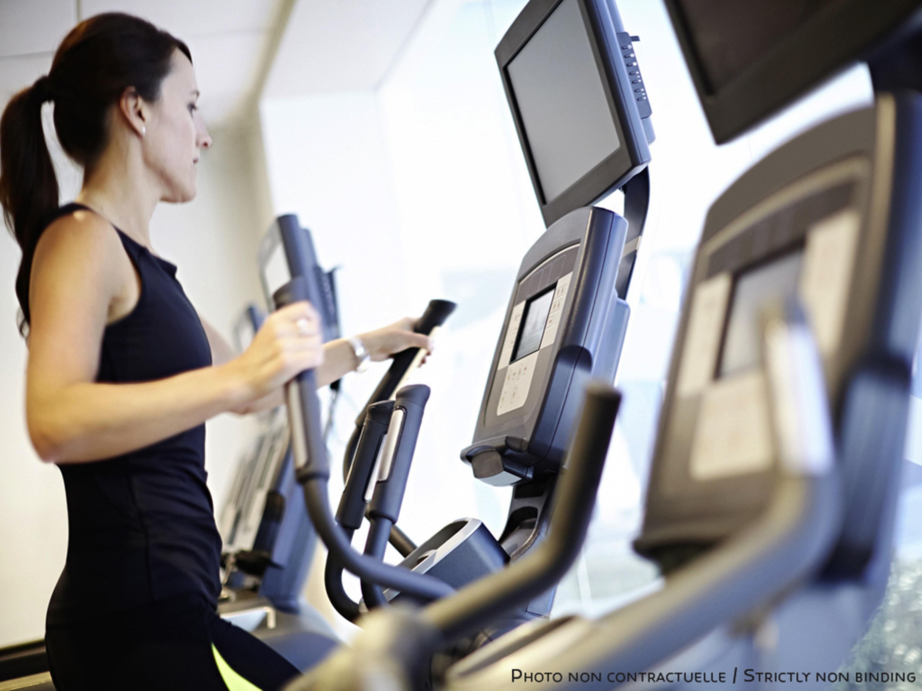 Novotel New Delhi Aerocity Екстериор снимка The photo shows a woman using elliptical machines in a gym or fitness center. She appears focused on her workout, dressed in athletic clothing. The machines feature digital screens, likely displaying workout statistics or options. The environment is 